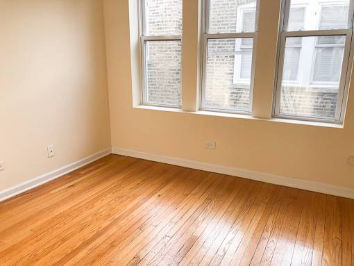 an empty room with wooden floors and three windows