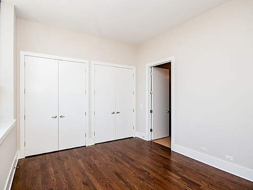 A room with white walls and wooden floors has three white cupboards with doors and drawers.