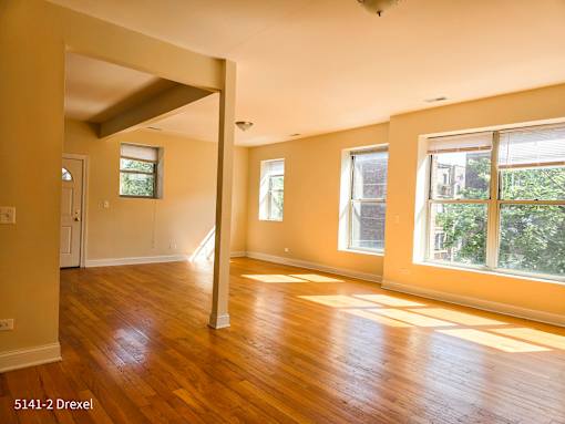 an empty living room with a hard wood floor and large windows
