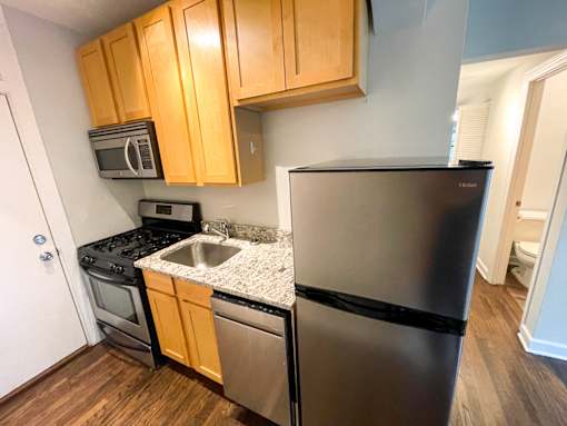 A kitchen with a black refrigerator, stainless steel sink, and wooden cabinets.
