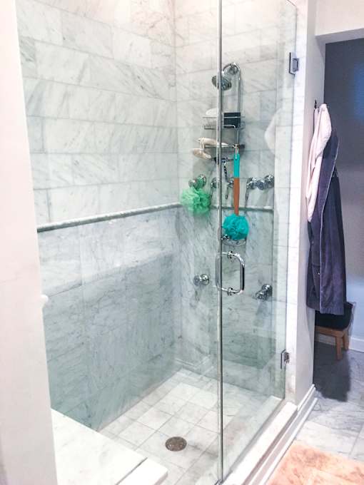 A shower with a glass door and a marble wall.