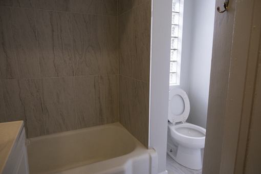 A white toilet is in a bathroom with a white tub.