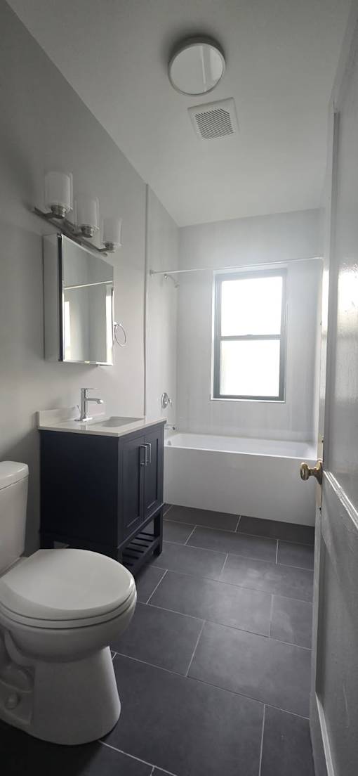 A white toilet sits in a bathroom with a black cabinet and a window.
