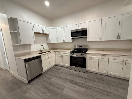 A kitchen with white cabinets and a grey floor.