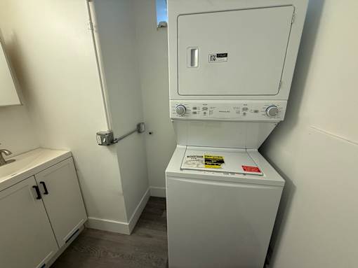 A white dryer is in a small room with a sink.