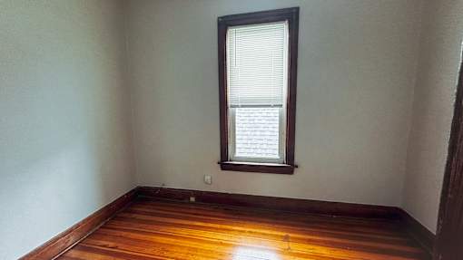 A room with a wooden floor and a window with blinds.