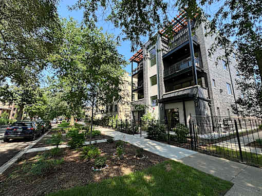A modern building with a balcony is surrounded by trees and a black fence.