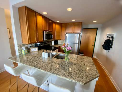A kitchen with granite countertops and white chairs.