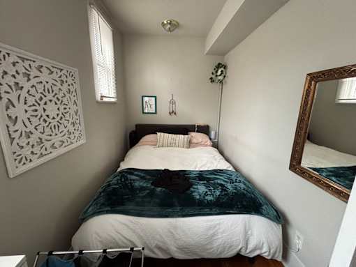 A bedroom with a bed, a mirror, and a decorative wall hanging.