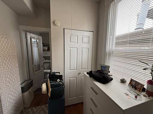 A white door is in a room with a white cabinet and a window with blinds.