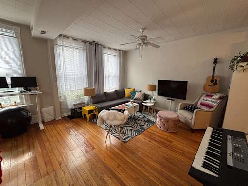 A living room with a couch, a chair, a table, a television, a guitar, a potted plant, and a keyboard.