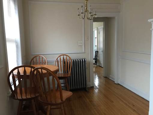 A room with a chandelier, a table with chairs, and a radiator.