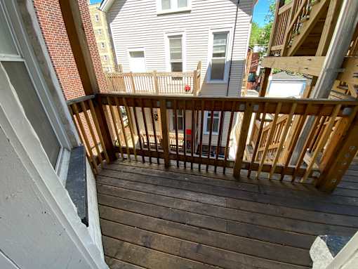 A wooden deck with a railing and a building in the background.