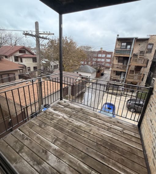 A balcony with a wooden floor and metal railing overlooks a residential area.