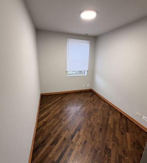 A room with wooden flooring and a window with blinds.