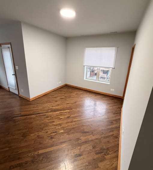 A room with wooden floors and a window with blinds.