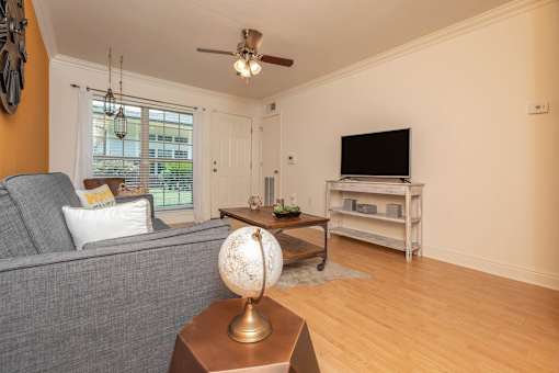 A living room with a grey couch, a wooden coffee table, and a television on a stand. at The Cove at State Street Apartments, Baton Rouge, LA