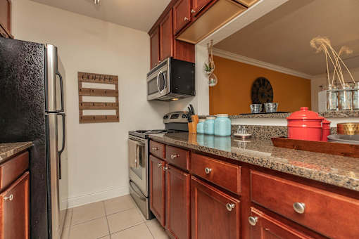 A kitchen with a black fridge, wooden cabinets, and a granite countertop. at The Cove at State Street Apartments, Baton Rouge, Louisiana