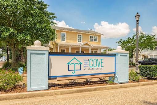 A sign for El Cove at State Street in front of a yellow house. at The Cove at State Street Apartments, Baton Rouge, LA