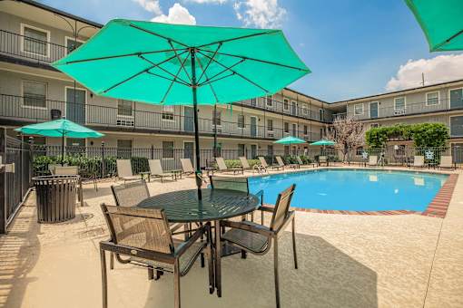 A table with chairs and umbrellas is set up by a pool. at The Cove at State Street Apartments, Louisiana, 70802
