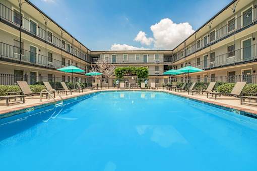 A large swimming pool in a resort with sun loungers and umbrellas. at The Cove at State Street Apartments, Baton Rouge, LA