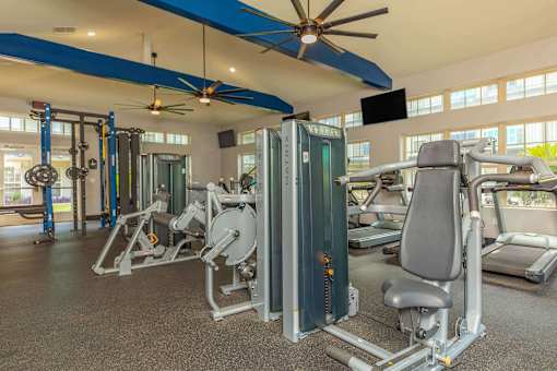 A gym with a variety of equipment including a weight machine and a bench press. at The Cove at State Street Apartments, Baton Rouge, LA