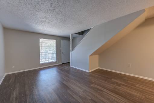 A room with wooden floors and a staircase leading to another room.