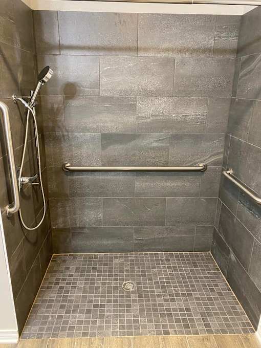 A shower with a tile floor and a tile wall.