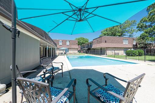 A pool area with chairs and a blue umbrella.