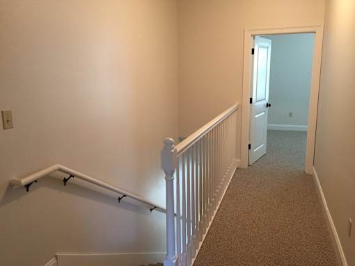 A hallway with a carpeted floor and white railings.