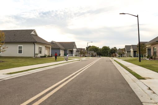 a street with houses on both sides and a person riding a bike down the street