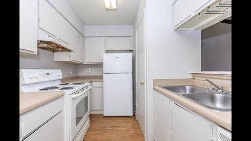 A white kitchen with a stove, refrigerator, and sink.