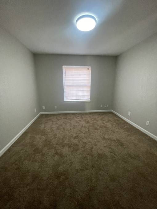 A room with a carpeted floor and a window with blinds.