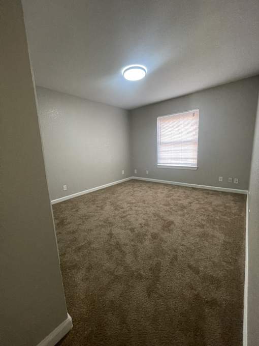 A room with a carpeted floor and a window with blinds.
