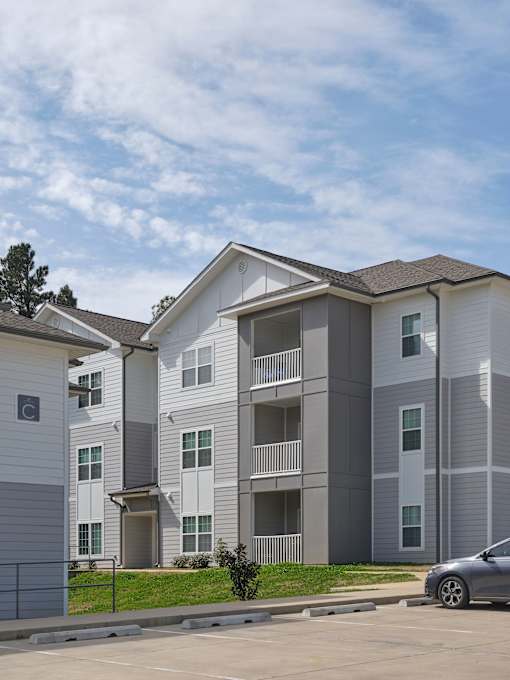 A grey and white apartment building with a car parked in front.