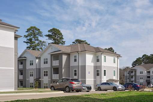 A grey apartment building with cars parked in front.