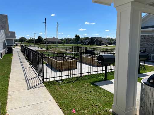 A black fence surrounds a grassy area with a white pillar on the right.