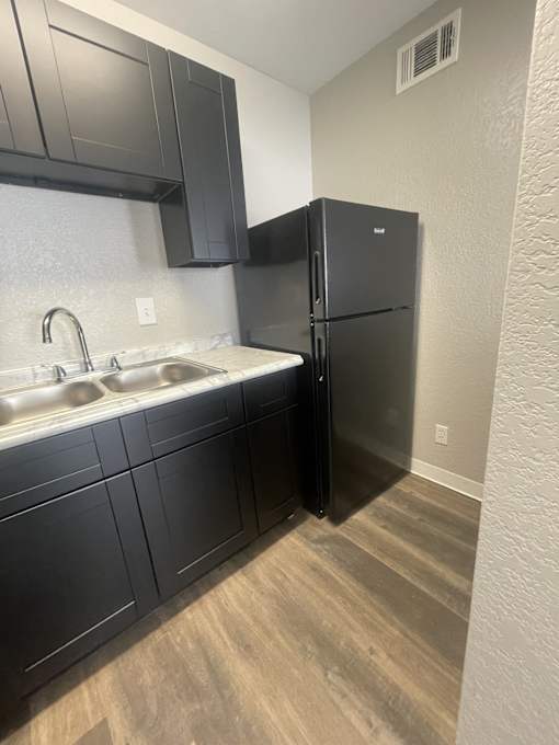 A black refrigerator in a kitchen with a white sink.
