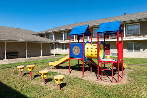 A playground with a slide, swings, and seesaw in front of a building.