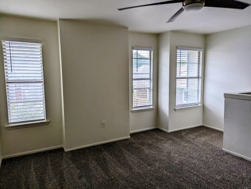 an empty living room with three windows and a ceiling fan