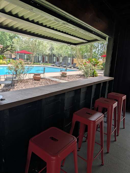 A row of red stools are lined up by a pool.