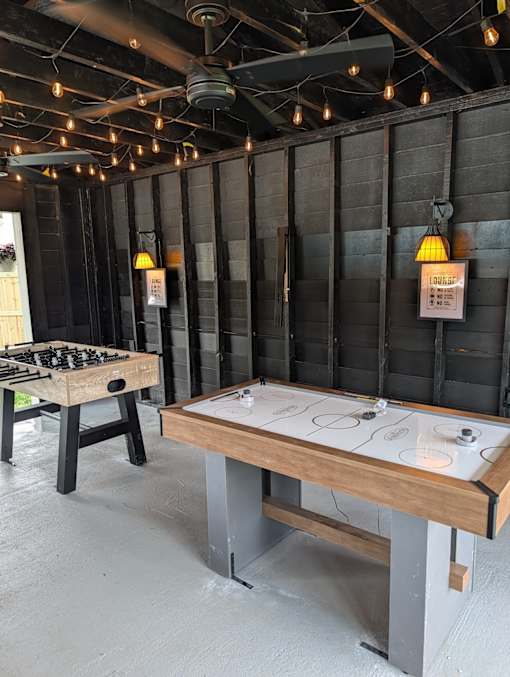 A shuffleboard table is in a room with a dark wood wall and a chess table.