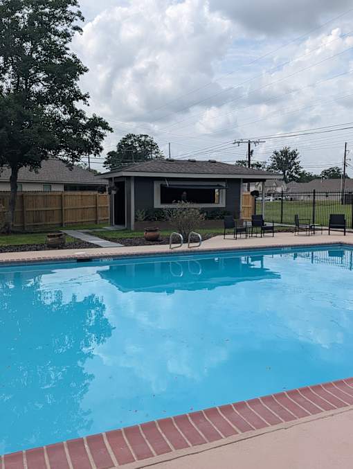 A pool with a red brick border and a house in the background.