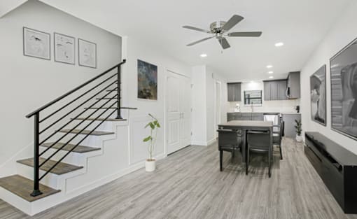 A modern interior with a staircase, a dining table, and a ceiling fan.