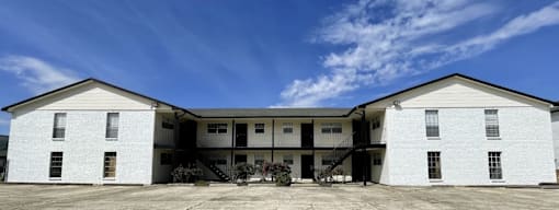 A white two-story building with a flat roof and a balcony on the second floor.
