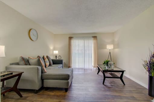 A living room with a grey couch, a coffee table, and a clock on the wall.