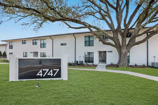 A sign with the number 4747 is in front of a building with a tree.