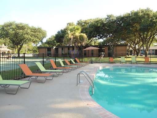 A pool with a metal fence and orange and green lounge chairs.