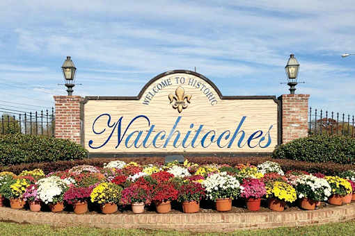 A sign that says Natchitoches surrounded by flowers.