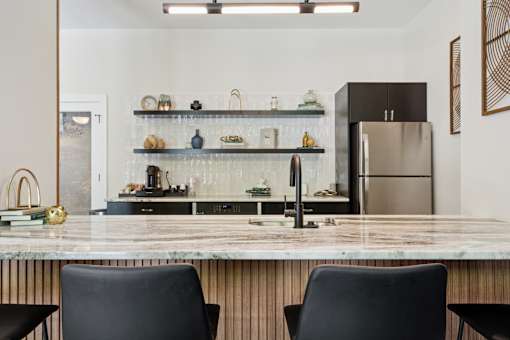 A modern kitchen with a marble countertop and black chairs.